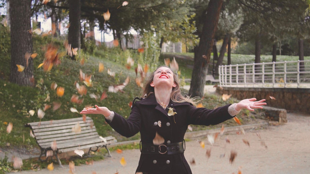 Mujer disfrutando caer las hojas en un parque. ¿Tu alegría refleja lo que guarda tu corazón? 3 Tips para lograrlo